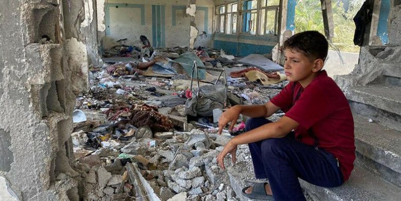 Menino sentado nos escombros de uma escola destruída da UNRWA em Nuseirat, Middle Areas,