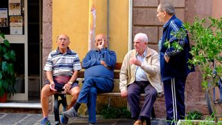 Quatro homens idosos sentam-se e conversam num banco