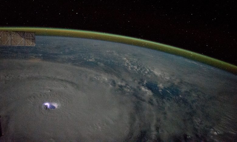 Uma foto da Terra vista da órbita mostrando um raio em um ciclone e a curvatura da Terra cercada por um brilho atmosférico dourado